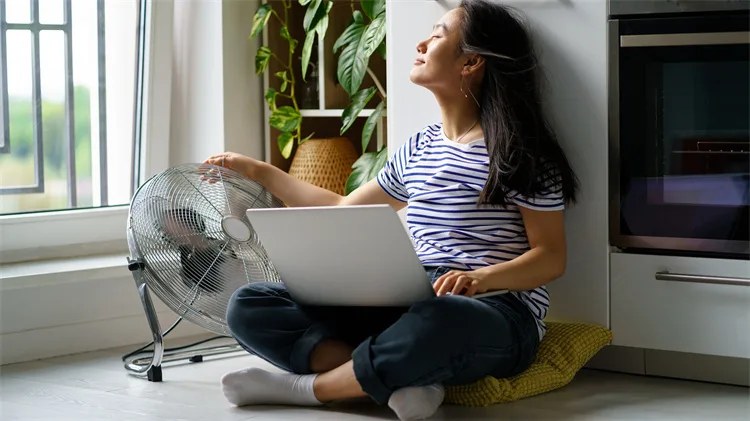 Woman enjoying cooling air from a fan at home